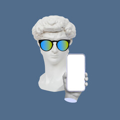 Antique David's statue head in sunglasses holding mobile phone with blank white screen demonstrating copy space for text or design isolated on blue color background. Contemporary art. Modern design
