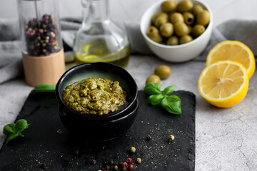 pesto sauce in a black bowl with olives, olive oil and basil. stone background. 