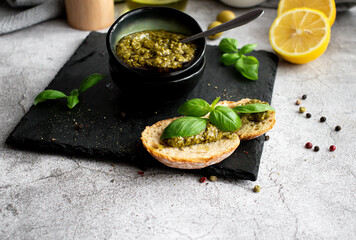 pesto sauce in a black bowl with olives, olive oil and basil. stone background. 