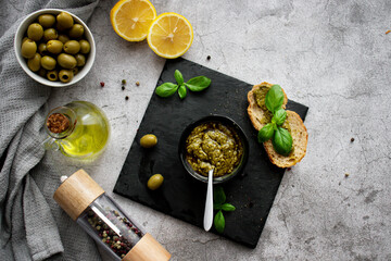 pesto sauce in a black bowl with olives, olive oil and basil. stone background. 