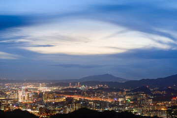 Blue sky with white dynamic clouds over the city at dusk at sunset. View of the urban landscape from Dajianshan Mountain, New Taipei City, Taiwan