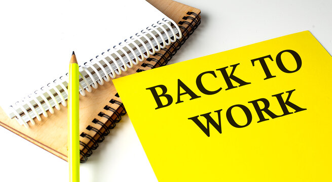BACK TO WORK text written on a yellow paper with notebook