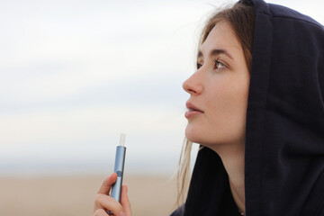 Electronic cigarette technology. Young woman smokes and releases steam from hybrid cigarette device...