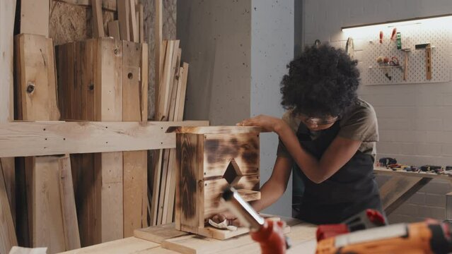 African American child polishing and wiping wooden birdhouse on table in carpentry studio alone