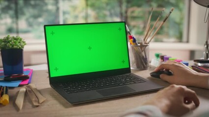 Over the Shoulder Footage with an Illustrator Using Laptop Computer with Mock Up Green Screen Chromakey Display. Art Student Sitting Behind a Desk, Browsing Online Lessons and Creative Tutorials