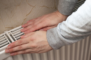 cold radiators, a woman touches the heating radiator with her hands, utility services are turned...