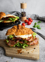 Croissant sandwich with bacon, egg and salad. on wooden board