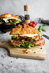 Croissant sandwich with bacon, egg and salad. on wooden board