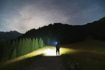 Papier Peint photo Tatras Night scene, the silhouette of a man with a headlamp goes hiking in the Tatra Mountains in summer.