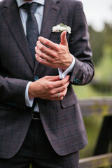 wedding details. The groom in a plaid suit straightens his cufflinks. Groom's blue tie. A man in a suit with a boutonniere. Platinum cufflinks.