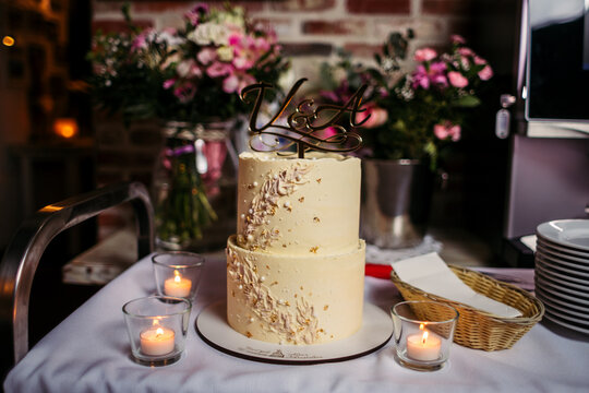 Wedding cake on the background of bouquets of flowers. The first letters of the names of the bride and groom on the cake. Wedding confectionery.
