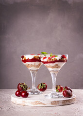 Summer cake in glass, strawberry sweet cherry layered trifle with biscuit, mascarpone and whipped cream on gray background