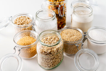 food storage, culinary and eating concept - close up of jars with different cereals, pasta and beans on white background