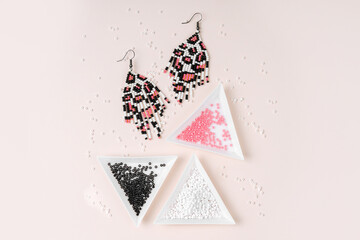 Triangular bead trays with beaded earrings. Different colored seed beads in containers for needlework and beading. Creativity and  hobby concept