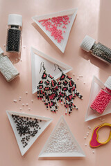 Triangular bead trays with beaded earrings. Different colored seed beads in containers for...