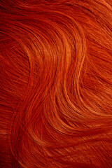 Red hair close-up as a background. Women's long orange hair. Beautifully styled wavy shiny curls. Hair coloring bright shades. Hairdressing procedures, extension.