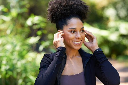 Beautiful multi-ethnic woman adjusts earphones before trail run in forest