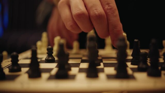 Close-up of thin female hands without manicure that rearrange the white piece of a horse on a filled chessboard in subdued light