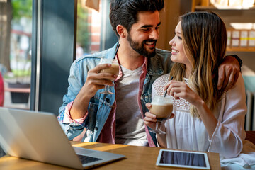 Couple sitting at cafe smiling, using laptop, spending time with pleasure, drinking coffee.