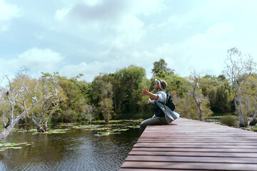 Fototapeta premium Asian man sitting and traveling on a bridge Take fun photos and videos. Rivers and mangroves