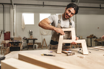 Young man carpenter wearing uniform working in joinery making wooden furniture