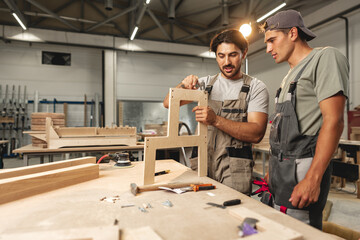 Two young men carpenters making furniture in warehouse of wood factory
