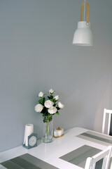 Modern stylish interior of dining room in soft pastel colors with white furniture and rose bouquet in vase on the table in an apartments