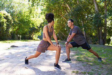 Beautiful couple stretch together before running in park, runners lunge