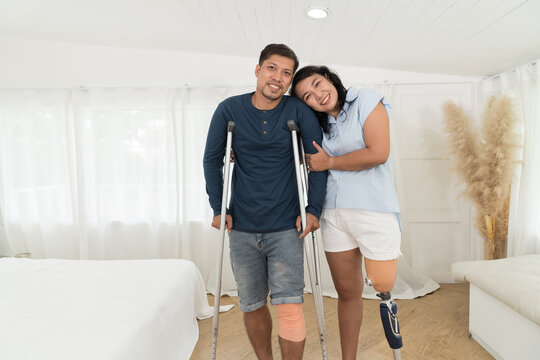 Happy smiling Asian woman with prosthetic leg embracing mature man during using crutches