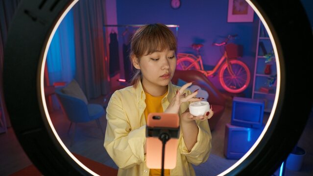 Young girl beauty blogger in casual holding a face cream jar in front of the camera at home studio.