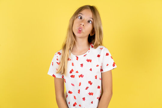 blonde kid girl wearing polka dot shirt over yellow studio background making fish face with lips, crazy and comical gesture. Funny expression.