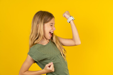 Profile photo of excited blonde kid girl wearing green T-shirt over yellow studio background good...