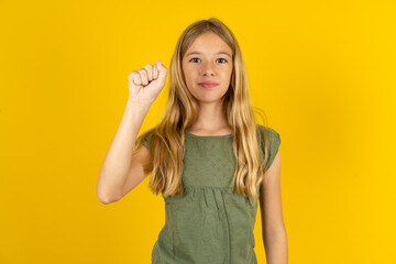 blonde kid girl wearing green T-shirt over yellow studio background pointing up with fingers number ten in Chinese sign language Shi