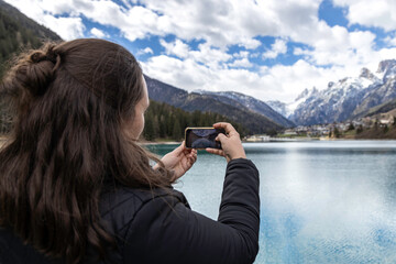 A female tourist taking a photo of Auronzo lake, in Auronzo di Cadore village; forest and dolomites...