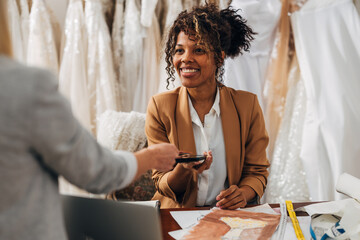 A Biracial woman works in a bridal salon and receives a contactless payment.