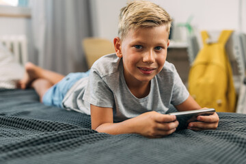 Cute young boy laying on the bed and using a mobile phone.