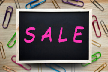Chalkboard inscription Sale. Message in chalk on the blackboard on blurred paper clips background. Top view on flat lay. Back to School Sales. Template for advertising, website, Stationery store