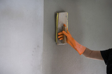 Worker hand wear orange gloves holding trowel spreading concrete.Empty cement concrete wall texture free space background.Abstract gray floor.Building concept.