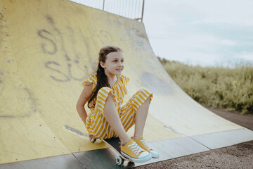 Mädchen, 9 Jahre, im gelbweiß gestreiften Jumpsuit mit Skateboard auf einer gelben Skaterbahn