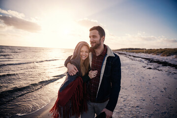 Young couple walking on a beach during winter at sunset
