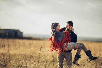 Young man carrying his girlfriend on a field in the countryside