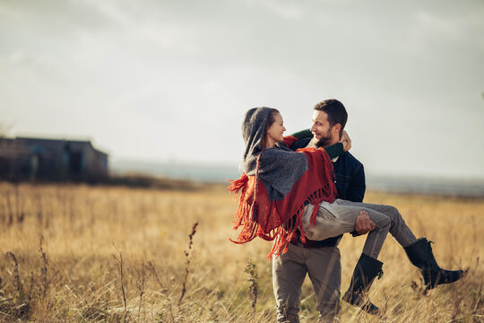 Young man carrying his girlfriend on a field in the countryside