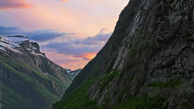 Vibrant twilight summer sunset on the Geiranger Fjord in Norway with dramatic with steep cliffs and snow capped mountains