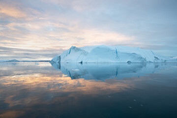 Fototapeta na wymiar Iceberg at sunset. Nature and landscapes of Greenland. Disko bay. West Greenland. Summer Midnight Sun and icebergs. Big blue ice in icefjord. Affected by climate change and global warming concept.
