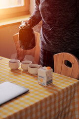 Concept of the cosy family morning. A woman is pouring the water into the cups with tea bags inside. Concept of the family breakfast. Priceless atmosphere. Calm morning.