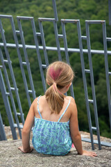 Girl looks through railing on mountain in summer with pink heart in hair
