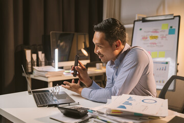 Obraz na płótnie Canvas Young Asian businessman talking on the phone late night hustle ambitious Working overtime talking on the phone in the organization