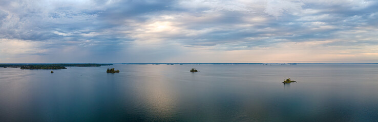 Aerial panorama taken late in the day above a very large lake that has small islands. The calm lake is reflecting the blue and yellow colors of the clouds.
