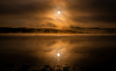 sunrise in the middle of the mountains with a orange sun, and lake with blue water. Cloudy morning 