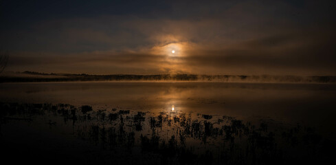 sunrise in the middle of the mountains with a orange sun, and lake with blue water. Cloudy morning 